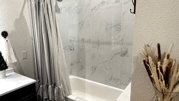 A bathroom with a bathtub, a shower curtain, and a vase with dried plants.