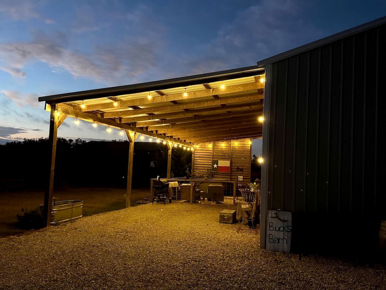An outdoor covered area with a barbecue setup, a flag, and a sign that reads 'Bucks Barn.'