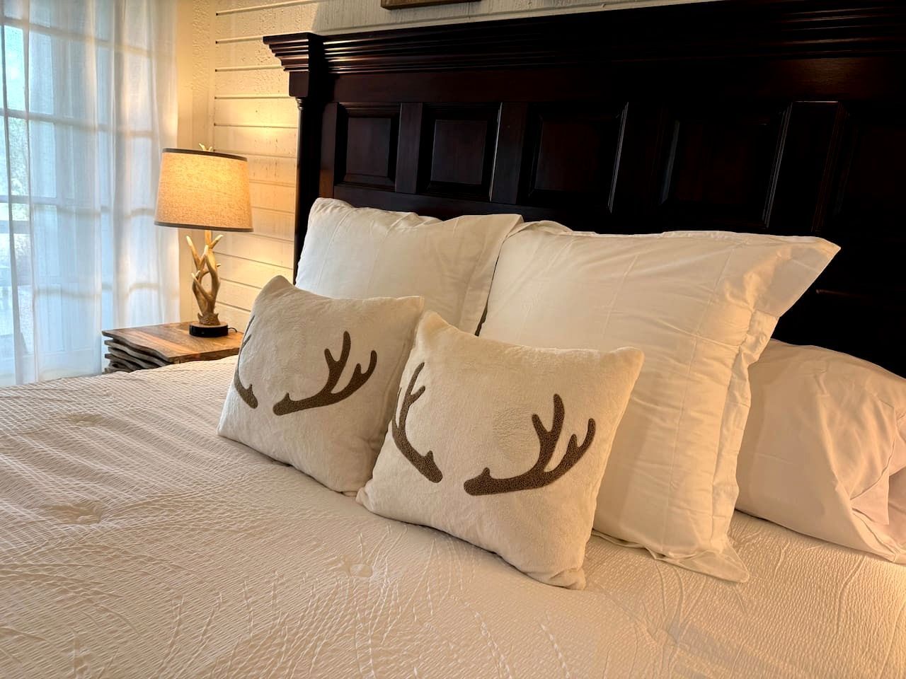A bed with white bedding and two decorative pillows with reindeer antlers.