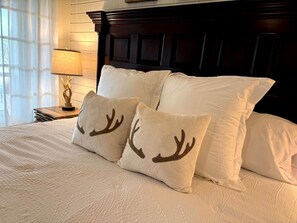 Una cama con ropa de cama blanca y dos almohadas decorativas con cuernos de ciervo.