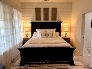 A large bed with a dark headboard, two bedside lamps, and decorative wall panels. - Charming Buck’s Barn Rustic Retreat with Patio and Private Hot Tub Near Spring Creek in Fredericksburg, Texas (Fredericksburg)