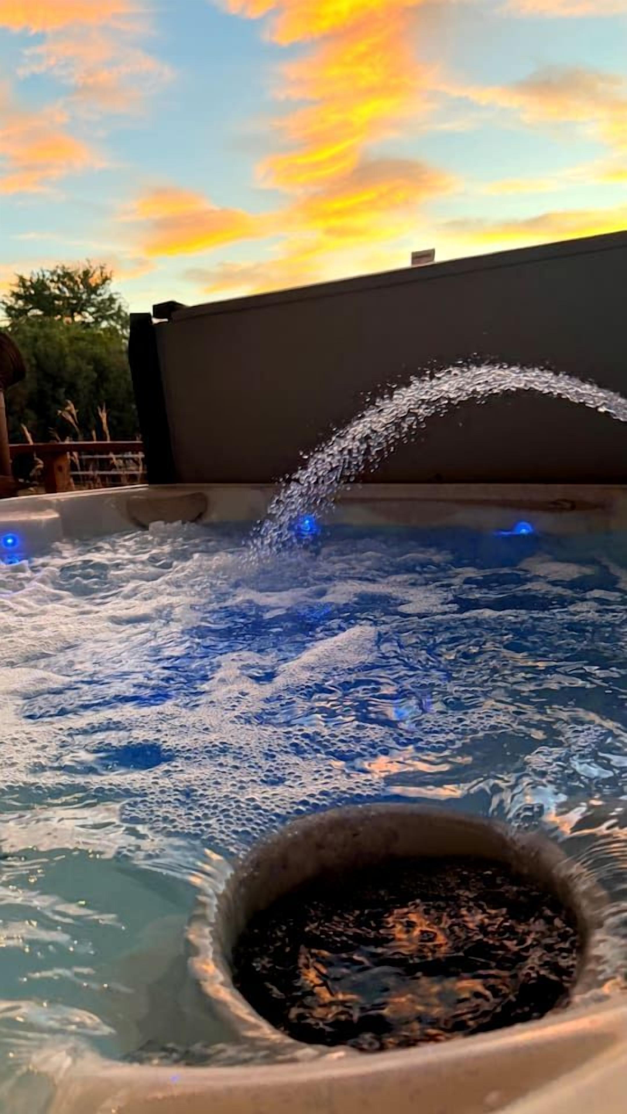 A hot tub with water jets, surrounded by a pool, under a sunset sky.