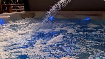 A hot tub with water jets, surrounded by a pool, under a sunset sky.