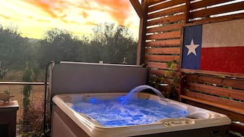 A hot tub with a Texas flag backdrop, surrounded by wooden slats and a view of trees.