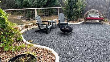A backyard with a fire pit, Adirondack chairs, and a wooden bench.