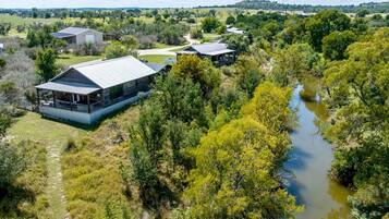 A modern building with a metal roof, surrounded by lush greenery and a river.