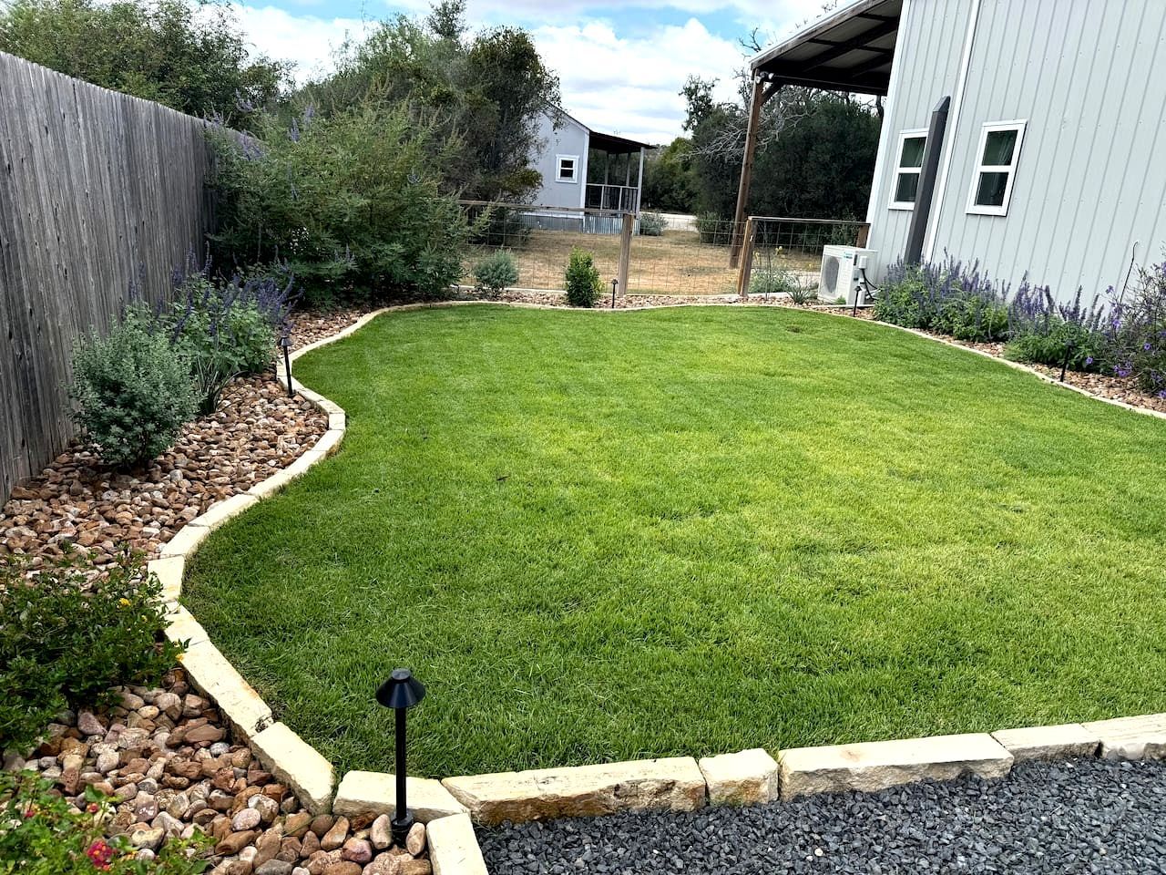 A well-maintained lawn with a stone border, a wooden fence, and a building in the background.