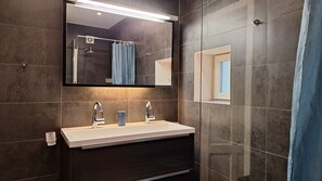 Ein modernes Badezimmer mit großem Spiegel, zwei Waschbecken, einer Dusche und einem Fenster.