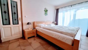 A bedroom with a bed, bedside table, lamp, and a window with curtains.