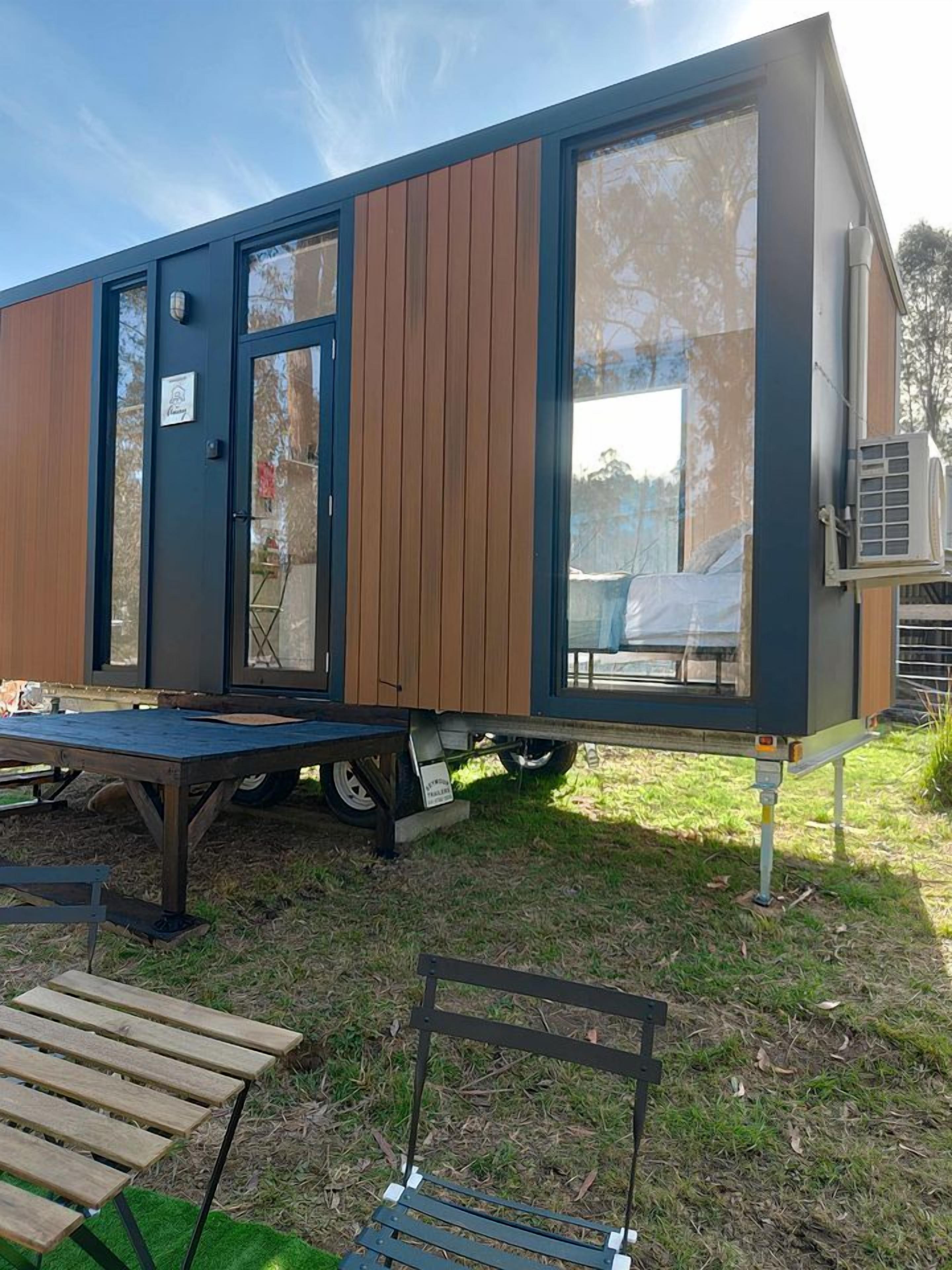A modern, compact mobile home with a large sliding door, a small deck, and a bench.