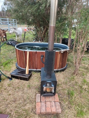 A hot tub with a wooden exterior, a metal chimney, and a brick base.