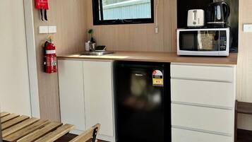 A compact kitchenette with a microwave, toaster, and coffee maker. There is a small refrigerator, a fire extinguisher, and a window above the sink.