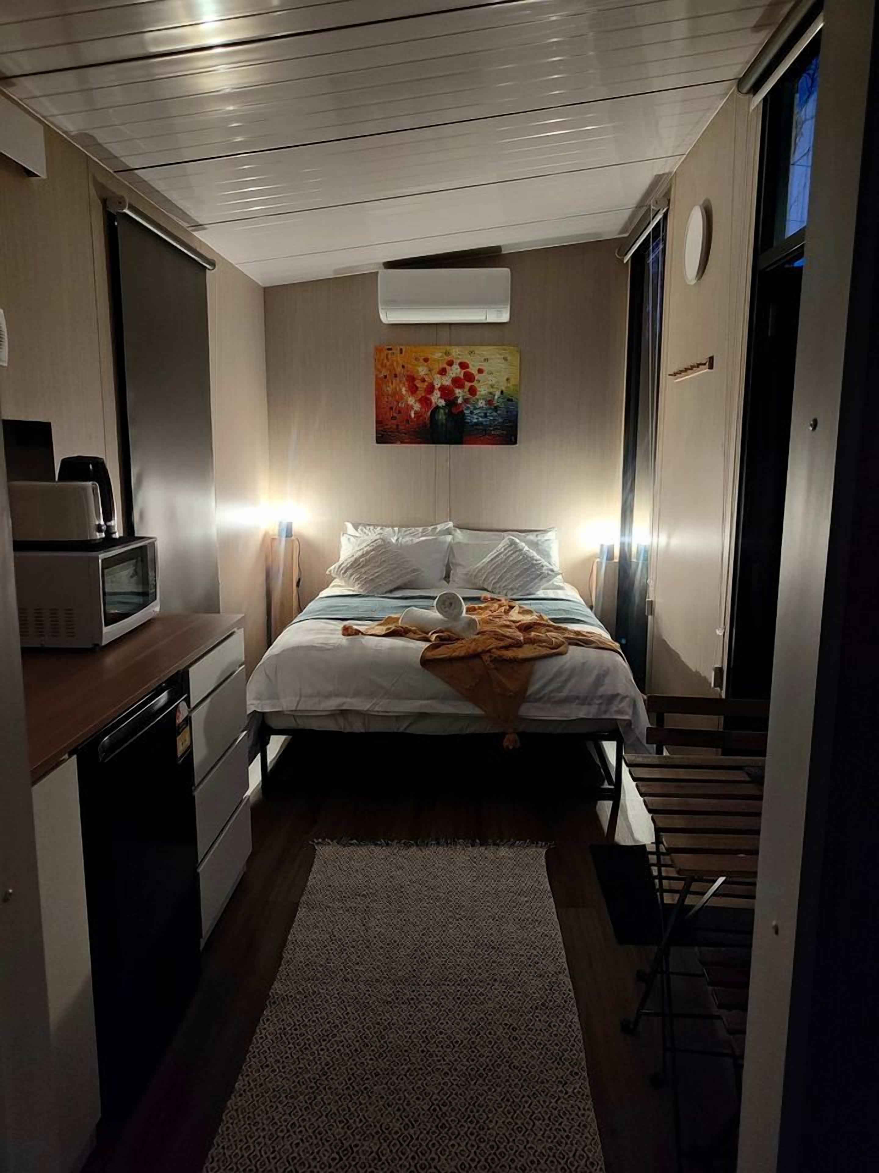 Une chambre d’hôtel de taille réduite, comprenant un lit, une table de chevet, un four à micro-ondes et un tableau au mur.