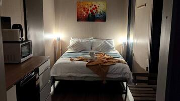 Ein kleines Hotelzimmer mit Bett, Nachttisch, Mikrowelle und einem Gemälde an der Wand.