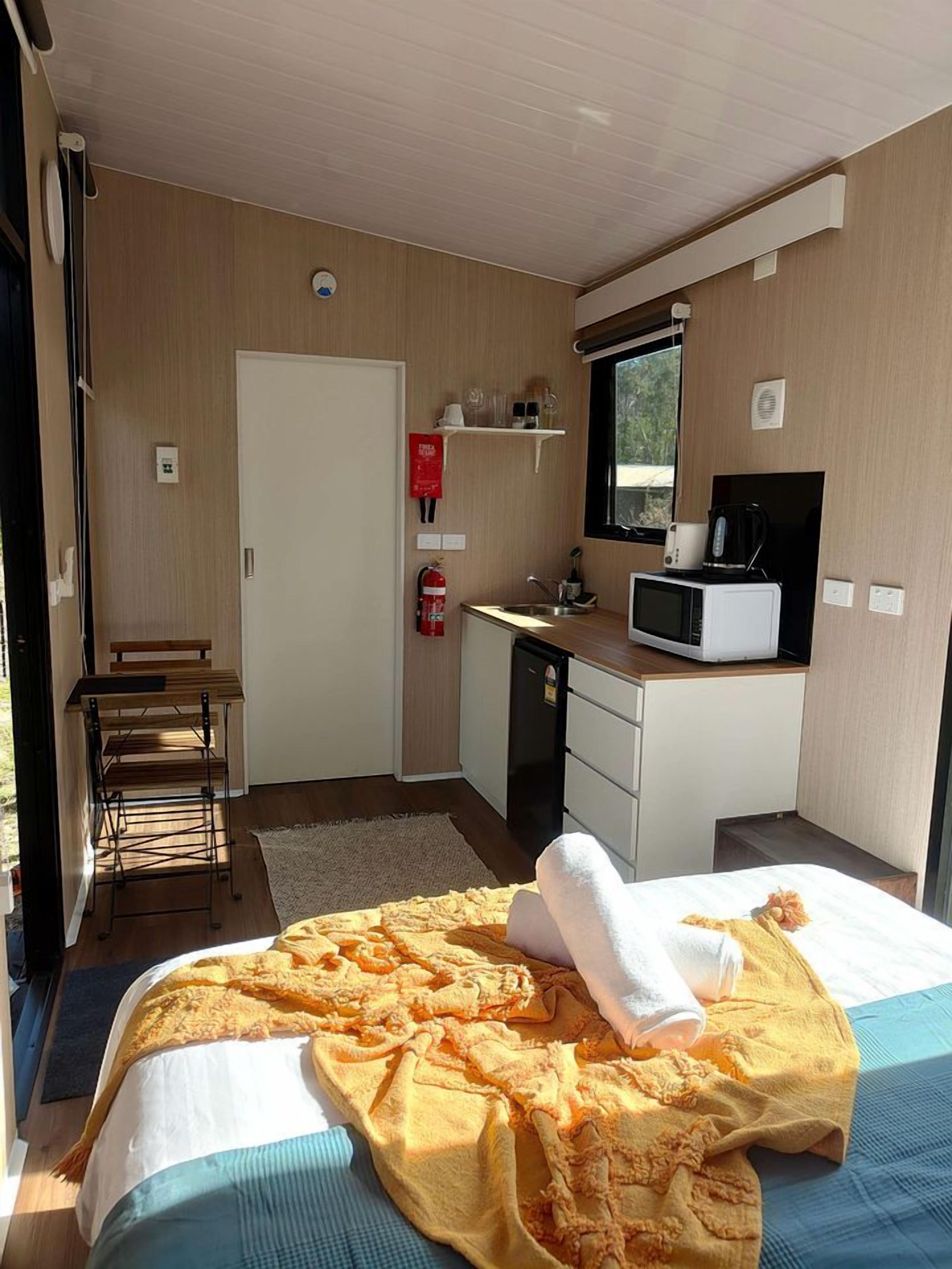 Une chambre avec un lit, une petite kitchenette, une fenêtre et un extincteur.