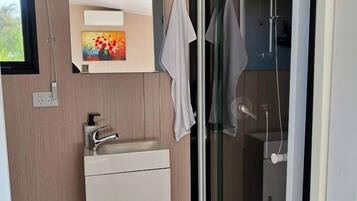Ein modernes Badezimmer mit einer Duschkabine aus Glas, einem weißen Waschbecken und einem Spiegel darüber.