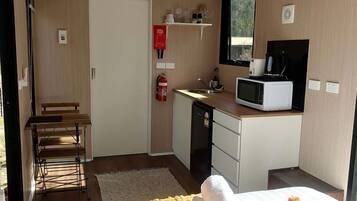 Ein Zimmer mit einem Bett, einer kleinen Küchenzeile, einem Fenster und einem Feuerlöscher.