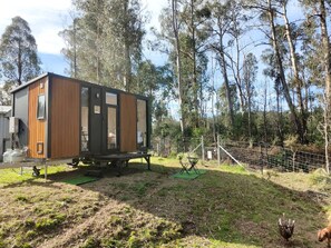 Una casa móvil con fachada de madera, una pequeña terraza y un patio cercado.