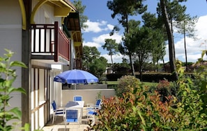 A hotel balcony with a wooden railing, a blue umbrella, and outdoor seating. - Les Greens Du Bassin (Gujan-Mestras)