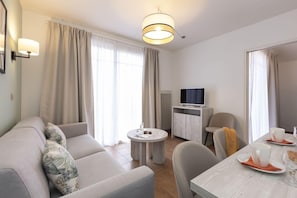 A modern living room with a sofa, a coffee table, a TV, and a dining area with chairs and a table. - Les Greens Du Bassin (Gujan-Mestras)