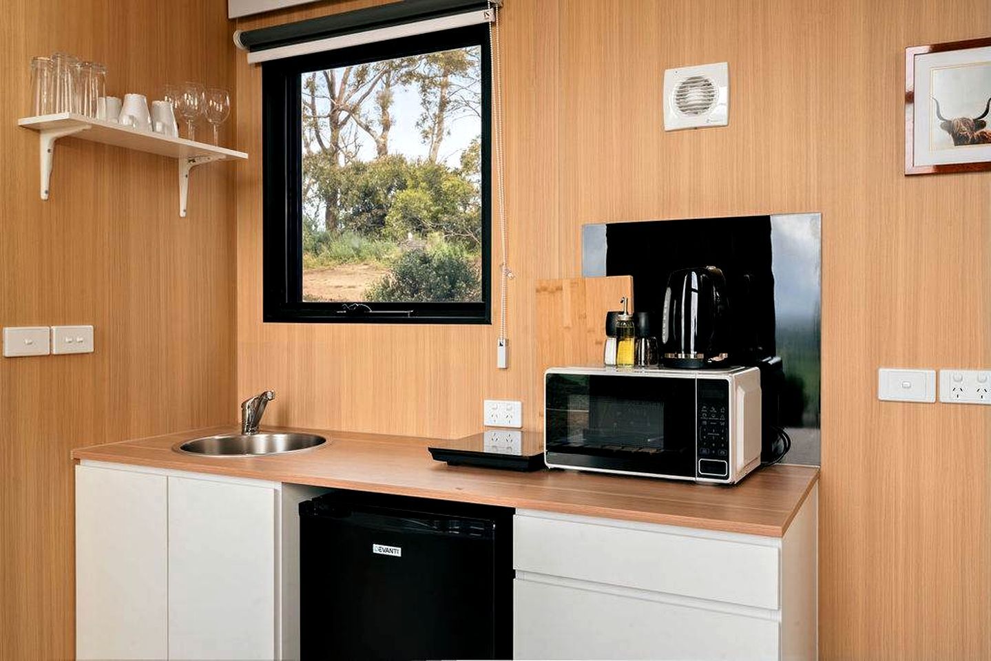 A compact kitchen with a built-in microwave, a coffee maker, and a window overlooking a natural landscape.