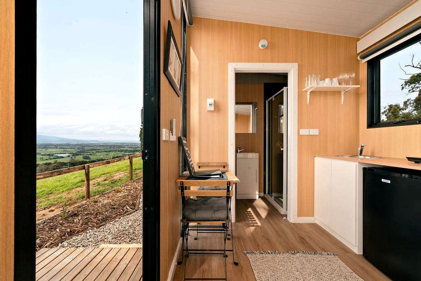 A modern kitchen with a view of a green landscape, a wooden dining area, and a black dishwasher.