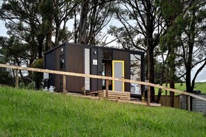 A small, dark-colored cabin with a yellow door, surrounded by trees and a grassy area.