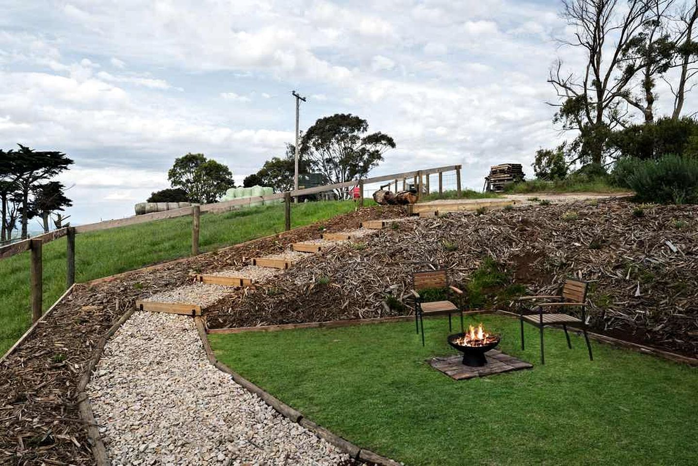 A landscaped outdoor area with a fire pit, seating, and a pathway leading uphill.
