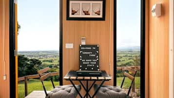 Een kamer met houten frame en uitzicht op het platteland, een welkomstbord en een tafel met twee fauteuils.
