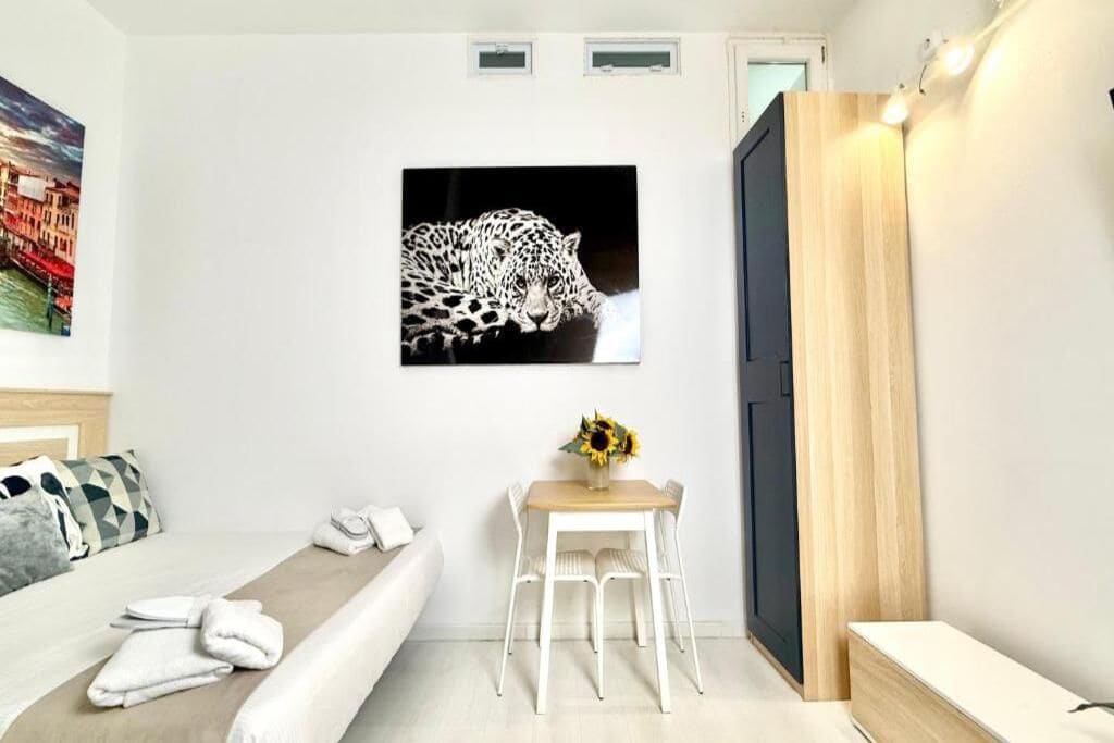 A hotel room with a bed, a desk with a chair, a painting of a leopard, and a wooden door.