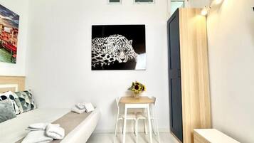 A hotel room with a bed, a desk with a chair, a painting of a leopard, and a wooden door.