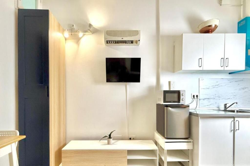 Une cuisine moderne avec des meubles blancs, un four à micro-ondes, un grille-pain et une petite plante posée sur une étagère en bois.