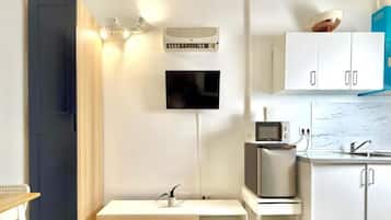 Una cocina moderna con armarios blancos, microondas, tostadora y una planta pequeña sobre una repisa de madera.