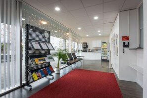 A reception area with a red carpet, seating, a reception desk, and a clock. - Hine Adon Apart Bern Airport (Belp)