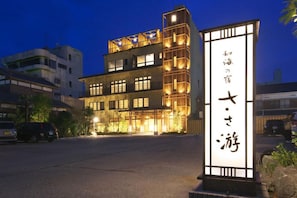 A multi-story hotel with illuminated signage and a parking lot in the foreground. - Sasayu (Shirako)