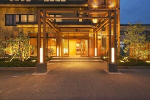 Un edificio moderno con acceso cubierto, iluminación exterior y zonas ajardinadas.