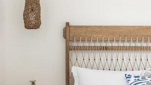 A bedroom with a wooden headboard, a hanging light fixture, a bedside table with a plant, and a patterned bedspread. - Saluti Da Stampalia (Astypalaia)