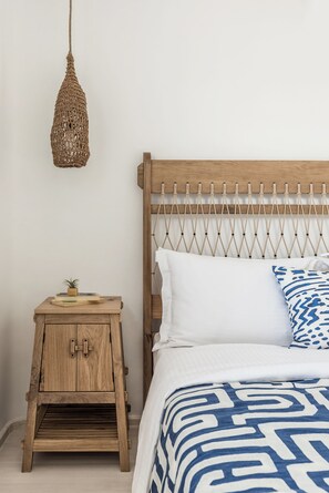 A bedroom with a wooden headboard, a hanging light fixture, a bedside table with a plant, and a patterned bedspread. - Saluti Da Stampalia (Astypalaia)