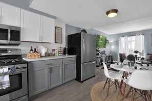 A modern kitchen with stainless steel appliances, a dining area with a round table and chairs, and a living space with a sofa and a TV. - Jackie's Green Parkside Mansfield Townhouse (Mansfield)