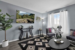 A living room with a large flat-screen TV, a potted plant, a round coffee table, and a sofa. - Jackie's Green Parkside Mansfield Townhouse (Mansfield)
