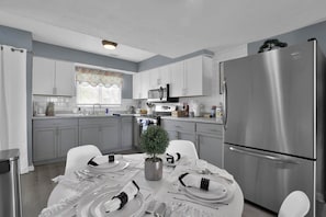 A modern kitchen with white cabinets, a stainless steel refrigerator, and a dining table set for four. - Jackie's Green Parkside Mansfield Townhouse (Mansfield)