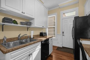 A kitchen with white cabinets, a granite countertop, a stainless steel sink, a black dishwasher, and a black refrigerator. - Hannah's Haus Historic German Village 3BR+Parking (Columbus)