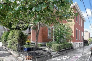 A residential building with a brick facade, a tree in the foreground, and a sidewalk with a metal fence. - Hannah's Haus Historic German Village 3BR+Parking (Columbus)