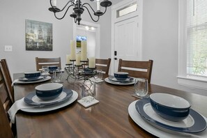 A dining table set with plates, bowls, and glasses, surrounded by chairs. - Hannah's Haus Historic German Village 3BR+Parking (Columbus)