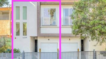 A two-story residential building with a garage, a balcony, and a fenced driveway.
