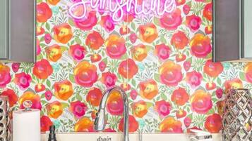 A kitchen with a vibrant floral backsplash, a stainless steel sink, and a 'Hello Sunshine' neon sign.