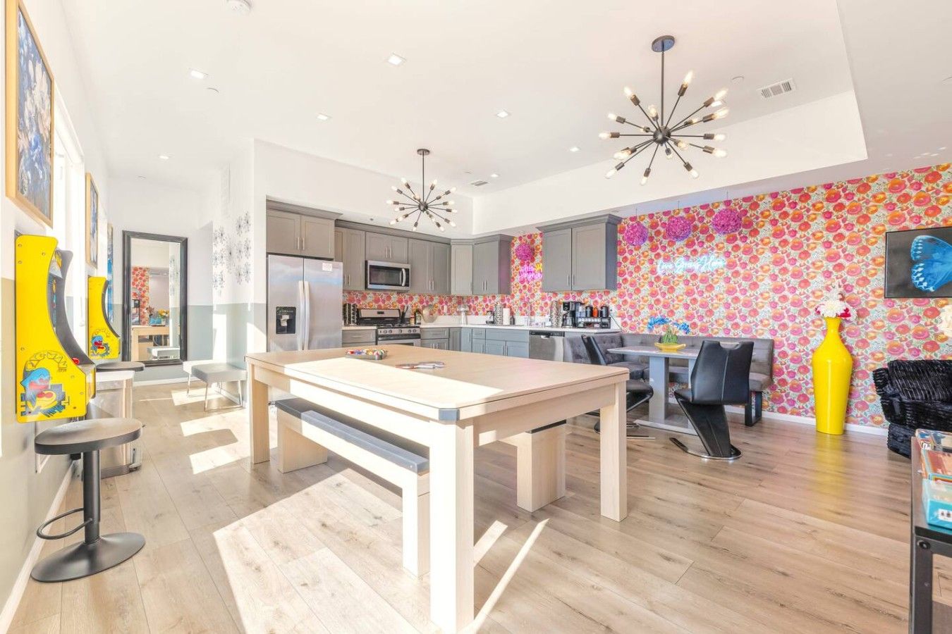 A modern kitchen with a central island, a dining area with a table and chairs, and a colorful floral wall.