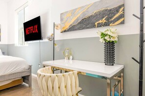 A modern hotel room with a bed, a desk with a vase of flowers, a wall-mounted TV, and a marble artwork.