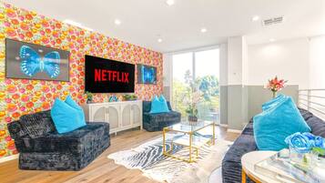 Un salón moderno con dos sofás, una mesa de centro y una pantalla de televisión mostrando 'NETFLIX'.