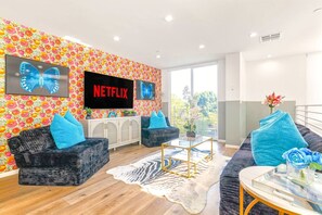A modern living room with two sofas, a coffee table, and a TV screen displaying 'NETFLIX'.